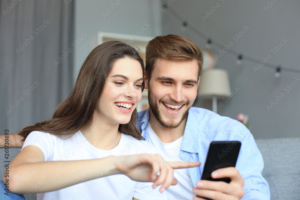 Young couple watching online content in a smart phone sitting on a sofa at home in the living room. Young couple watching online content in a smart phone sitting on a sofa at home in the living room.