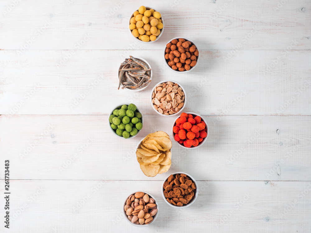 Assortment of different snack for beer, wine, party. Peanuts in coconut glaze, green vasabi, red spicy chilli, yellow cheese glaze, chips, pistachio, crackers, fish on white wooden table. Copy space Assortment of different snack for beer, wine, party. Peanuts in coconut glaze, green vasabi, red spicy chilli, yellow cheese glaze, chips, pistachio, crackers, fish on white wooden table. Copy space