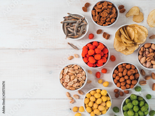 Assortment of different snack for beer, wine, party. Peanuts in coconut glaze, green vasabi, red spicy chilli, yellow cheese glaze, chips, pistachio, crackers, fish on white wooden table. Copy space