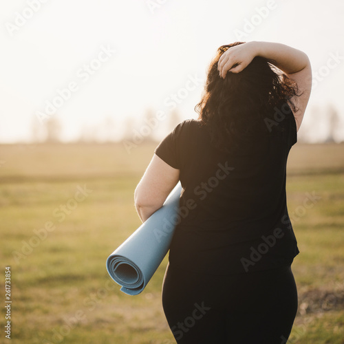 Active lifestyle, yoga, flexibility, sport, fitness, weight loss. Overweight woman with yoga mat before outdoor workout in nature