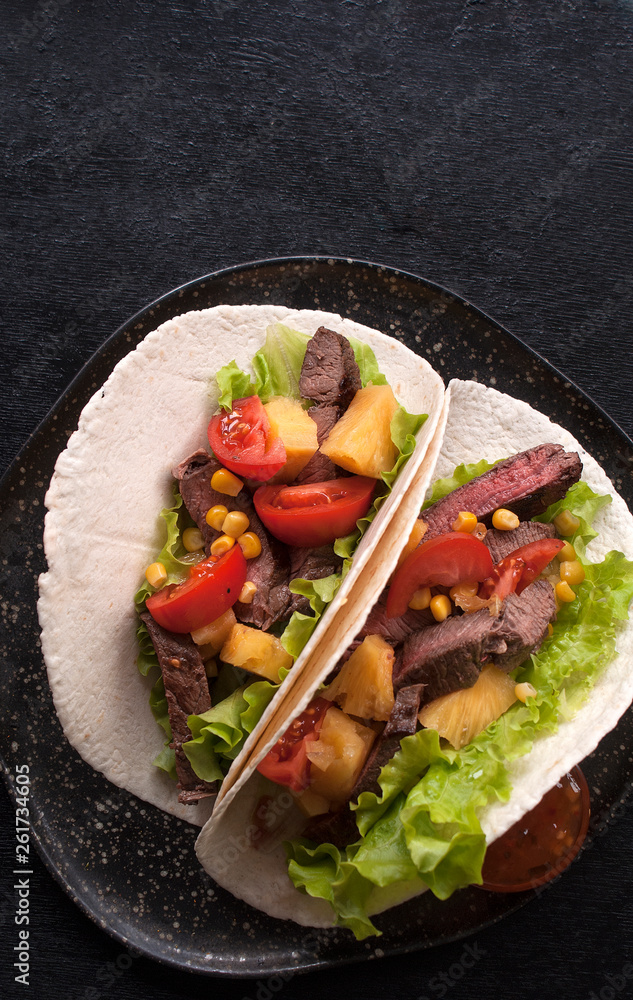 Mexican tacos with beef, vegetables and pineapples and corn grains. Taco al pastor on a wooden Board on a black background. Top view with copy space