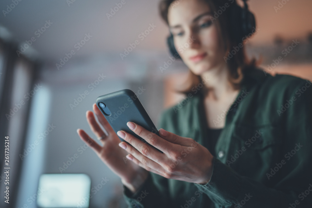 Young handsome girl relaxing at modern home,wearing casual clothes,playing music on smartphone and listening audio books in wireless headphones.Blurred background Young handsome girl relaxing at modern home,wearing casual clothes,playing music on smartphone and listening audio books in wireless headphones.Blurred background