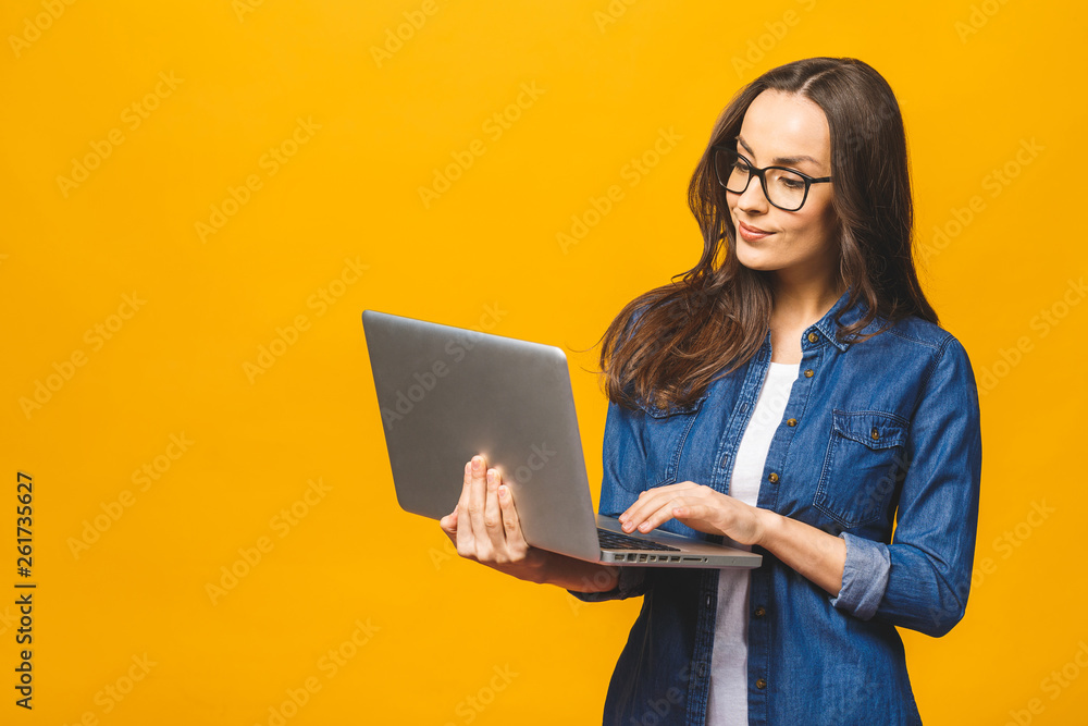 © denis_vermenko - Young happy smiling woman in casual clothes holding laptop and sending email to her best friend. Isolated against yellow background.