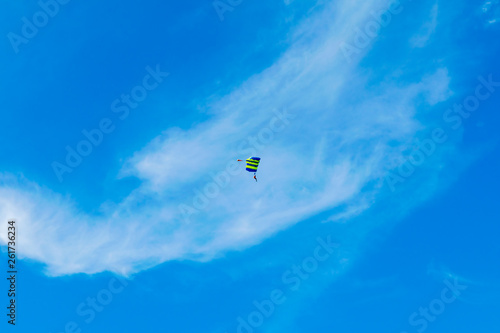 Male skydiver flies under the wing of the parachute, descending and coming in to land closer to the ground on a background of blue sky, white clouds