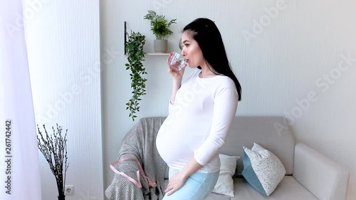 Pregnant woman drinking water. Healthy lifestyle. Expecting woman indoor. Pregnancy dehydration avoidance. female holding a glass of water. photo