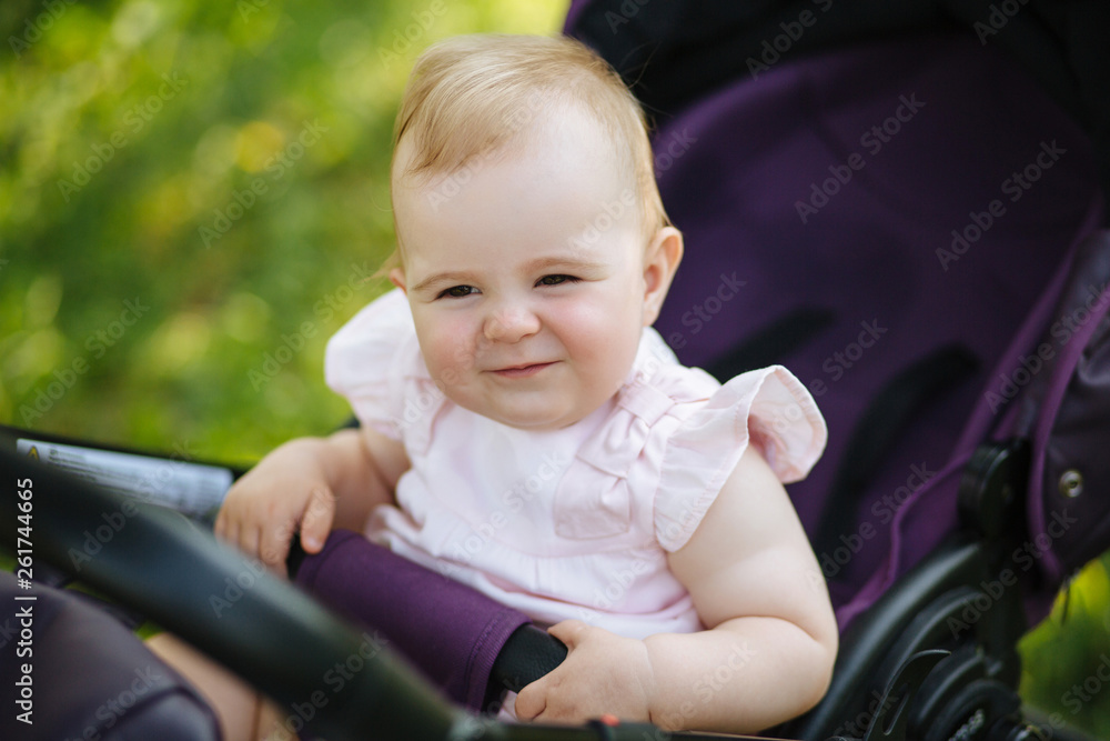 Cute little beautiful baby girl of 6 months sitting in the pram or stroller and waiting for mom Cute little beautiful baby girl of 6 months sitting in the pram or stroller and waiting for mom