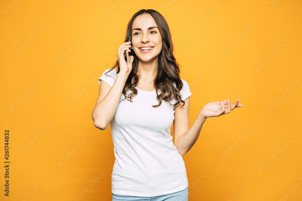 Hey-pass! Pretty girl in casual outfit of T-shirt and denim jeans is talking to her boyfriend by mobile phone next to spice orange wall. Hey-pass! Pretty girl in casual outfit of T-shirt and denim jeans is talking to her boyfriend by mobile phone next to spice orange wall.