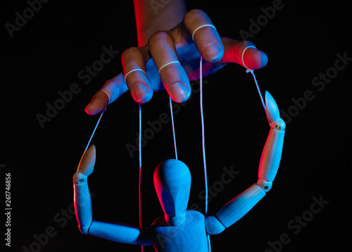 Concept of control. Marionette in human hand. Objects are colored on red and blue light. photo