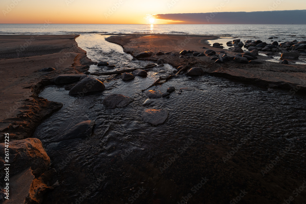 Beautiful sunset with red sand and spring water from a river exiting to the sea - Veczemju Klintis, Latvia - April 13, 2019