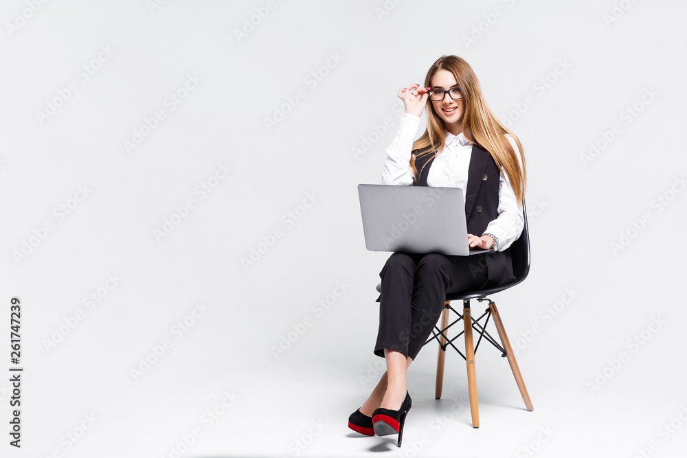 Young pretty woman enterprener working with notebook while sitting on black chair, isolated on gray! Copy space. Young pretty woman enterprener working with notebook while sitting on black chair, isolated on gray! Copy space.