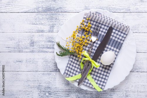 Easter table setting. White eggs, napkin on a plate, mimosa flowers, fork, knife on a wooden table