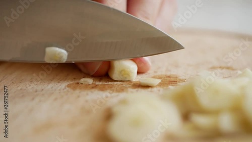 Slicing and dicing garlic cloves with a chef knife on a wooden kitchen board