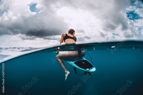 Attractive surf girl sit at surfboard in blue ocean