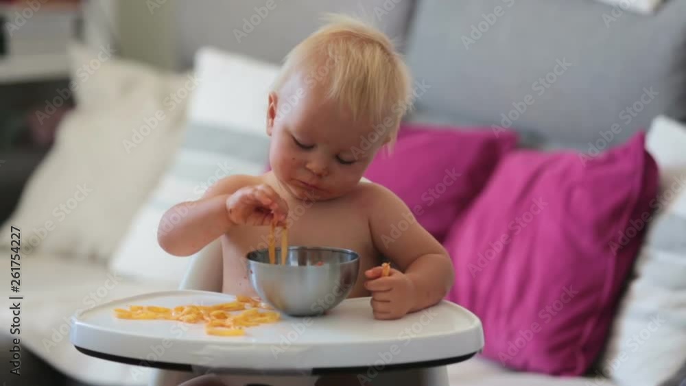 Adorable little baby one year old eating pasta indoor. Funny toddler child with spaghetti. Cute kid and healthy food Adorable little baby one year old eating pasta indoor. Funny toddler child with spaghetti. Cute kid and healthy food