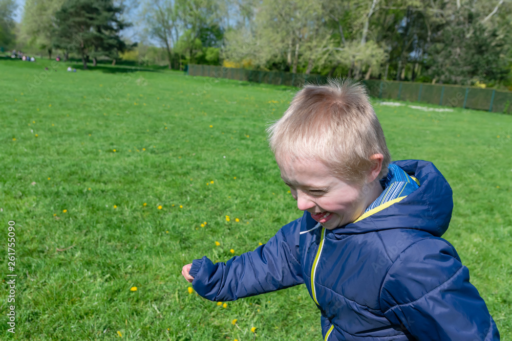 Defect,childcare,medicine and people concept: Blond boy with down syndrome playing in a park at spring time. Defect,childcare,medicine and people concept: Blond boy with down syndrome playing in a park at spring time.