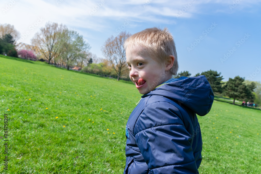  Defect,childcare,medicine and people concept: Blond boy with down syndrome playing in a park at spring time.
