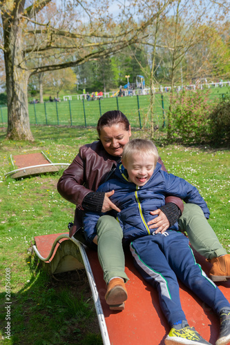 Defect,childcare,medicine and people concept: Happy mother and son with down syndrome playing together in a park at spring time.