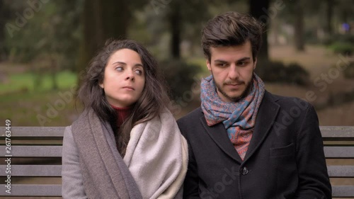 Shy young couple flirting and kissing sitting on park bench. First date