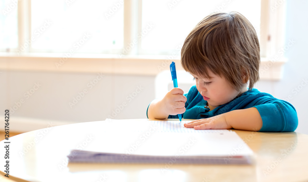 Toddler boy drawing with pen and paper at his desk Toddler boy drawing with pen and paper at his desk