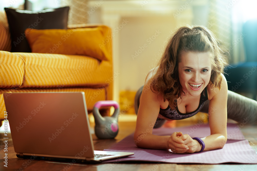 woman using online fitness site in laptop and doing exercises woman using online fitness site in laptop and doing exercises