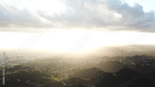 AERIAL: looking directly at the sun while sitting over the mountainous terrain of Hollywood during a sunset.