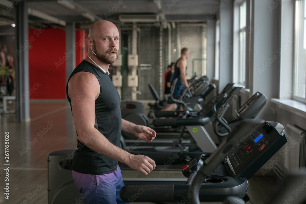 Fototapeta premium Fit Muscle bald Man With Headphones Running on Treadmill in Gym.