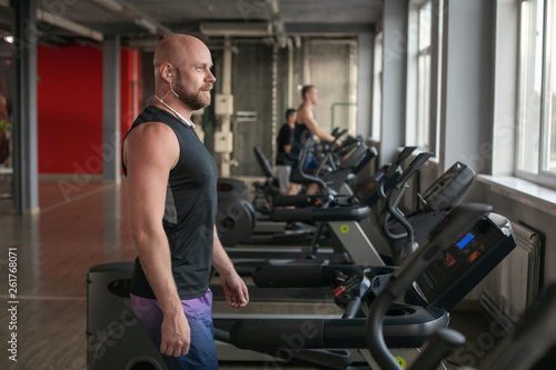 Fit Muscle bald Man With Headphones Running on Treadmill in Gym.