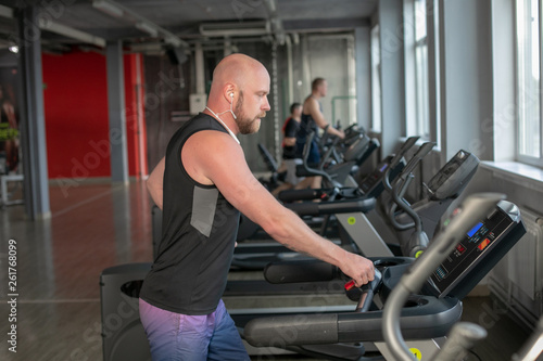 Fit Muscle bald Male With Headphones Running on Treadmill in Gym.