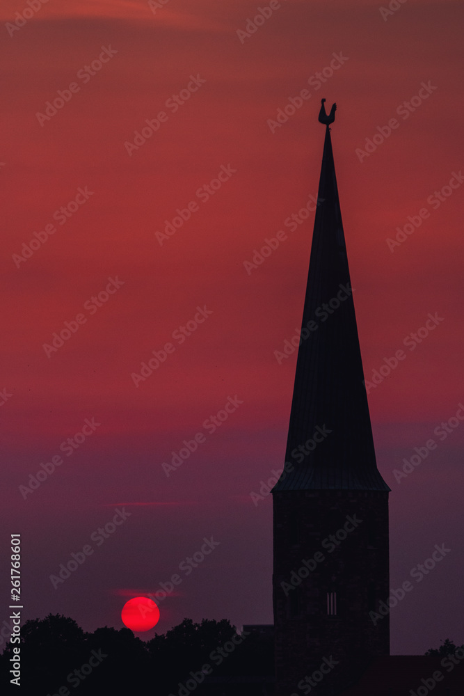 Fototapeta premium Beautiful and colorful summer sunset roof top view of a old historic church tower above the city. Warm red and orange sky color tones. Old town of Braunschweig, Germany