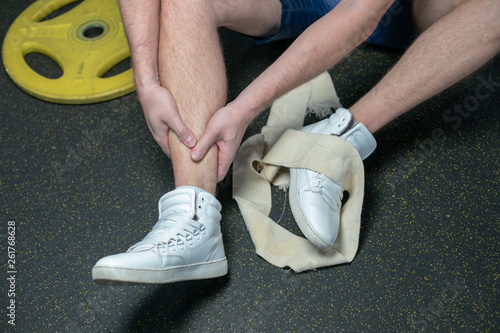 Sportsman in the white sneakers having pain in leg after exercise. close up. focus is on leg.
