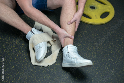 Sportsman in the white sneakers having pain in leg after exercise. close up. focus is on leg.