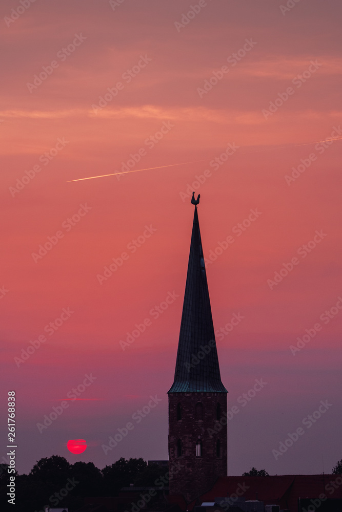 Beautiful and colorful summer sunset roof top view of a old historic church tower above the city. Warm red and orange sky color tones. Old town of Braunschweig, Germany