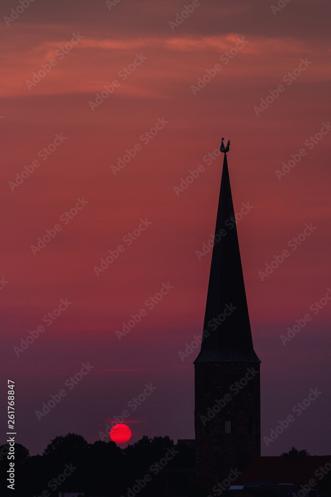 Fototapeta premium Beautiful and colorful summer sunset roof top view of a old historic church tower above the city. Warm red and orange sky color tones. Old town of Braunschweig, Germany
