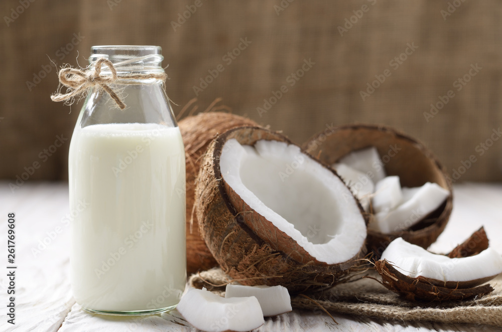 Glass bottle of milk or yogurt on hemp napkin on white wooden table with coconut aside Glass bottle of milk or yogurt on hemp napkin on white wooden table with coconut aside