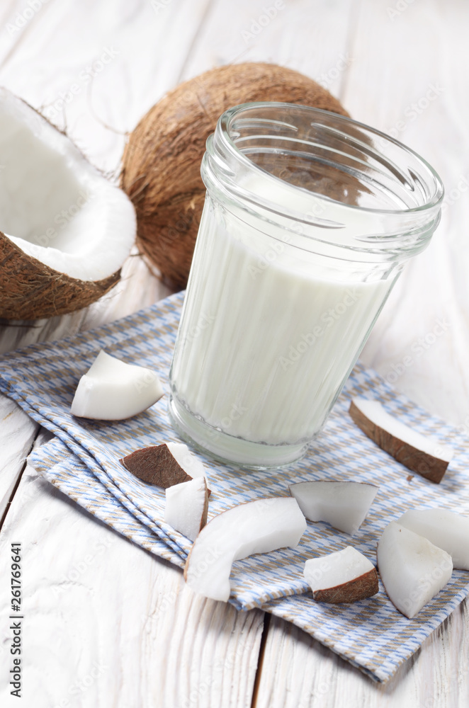 Mason jar of milk or yogurt on blue napkin on white wooden table with coconut aside Mason jar of milk or yogurt on blue napkin on white wooden table with coconut aside