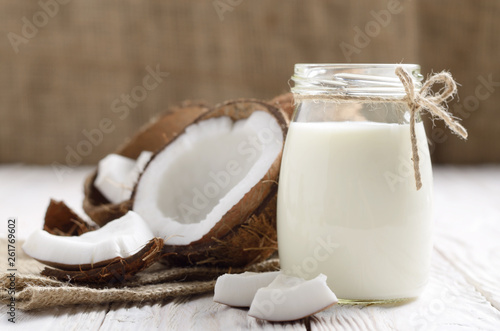 Mason jar of milk or yogurt on hemp napkin on white wooden table with coconut aside photo
