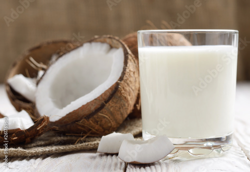 Drinking glass of milk or yogurt on hemp napkin on white wooden table with coconut aside