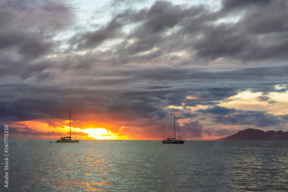 Two sailing boats over dark clouds background and orange sunset sea