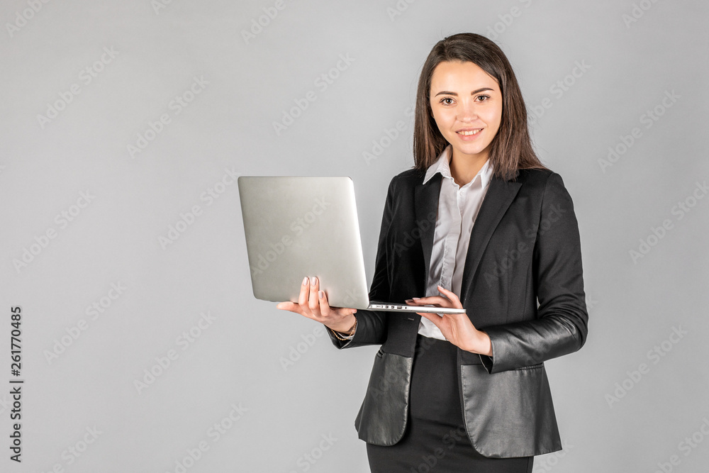 Photo of a young cheerful business woman standing over a gray wall with a laptop Photo of a young cheerful business woman standing over a gray wall with a laptop