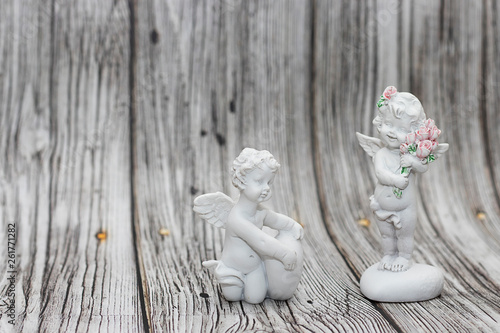 Figurines of angels on a wooden background. A boy with a heart and a girl with flowers standing on a heart.