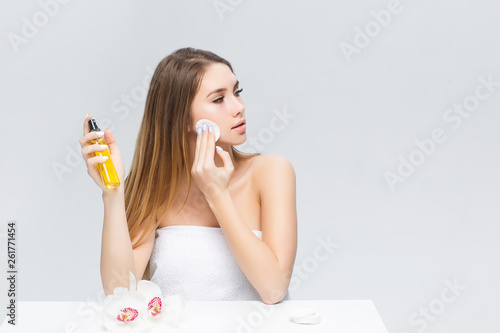 Gorgeous girl with brown hair fixed behind,clean fresh skin, big eyes and naked shoulders holding a cosmetic cleaning sponge, posing at gray studio background.