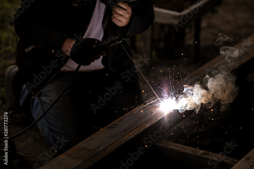 A caucasian worker works with a welding machine. Clip. Welding steel structures in the factory. Beautiful sparks fly out