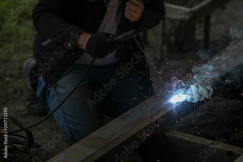 A caucasian worker works with a welding machine. Clip. Welding steel structures in the factory. Beautiful sparks fly out
