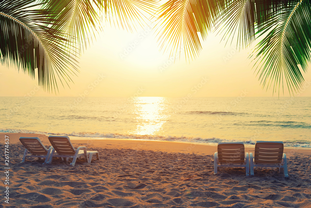 Beach chairs with coconut leaves on the tropical beach at sunset. Summer travel concept.