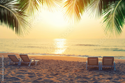 Beach chairs with coconut leaves on the tropical beach at sunset. Summer travel concept. © tawanlubfah