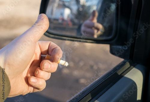 closeup of male hand with the missing finger holding a cigarette in a car in a residential area