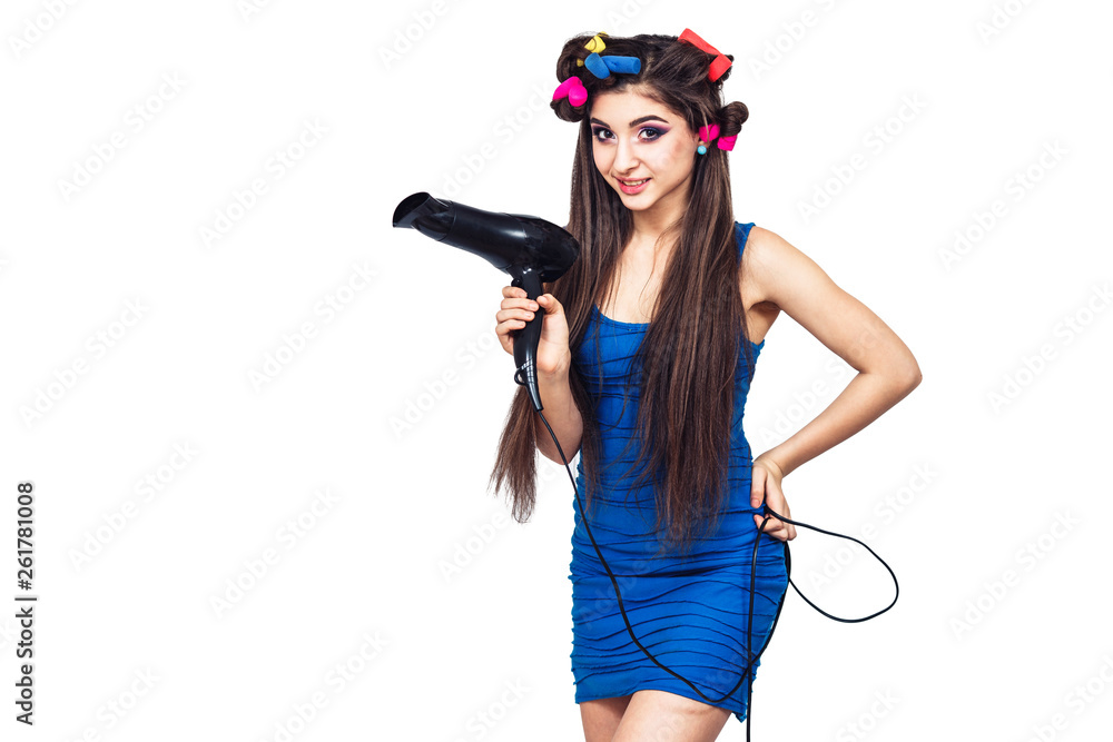 cute cheerful young girl in blue dress with hair curlers in her hair and with hairdryer in her hand. cute cheerful young girl in blue dress with hair curlers in her hair and with hairdryer in her hand.