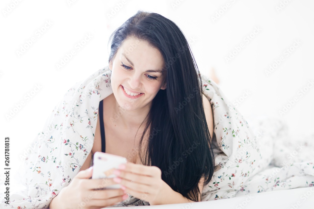 Black haired sexy woman relaxing and using white cell phone on bed.