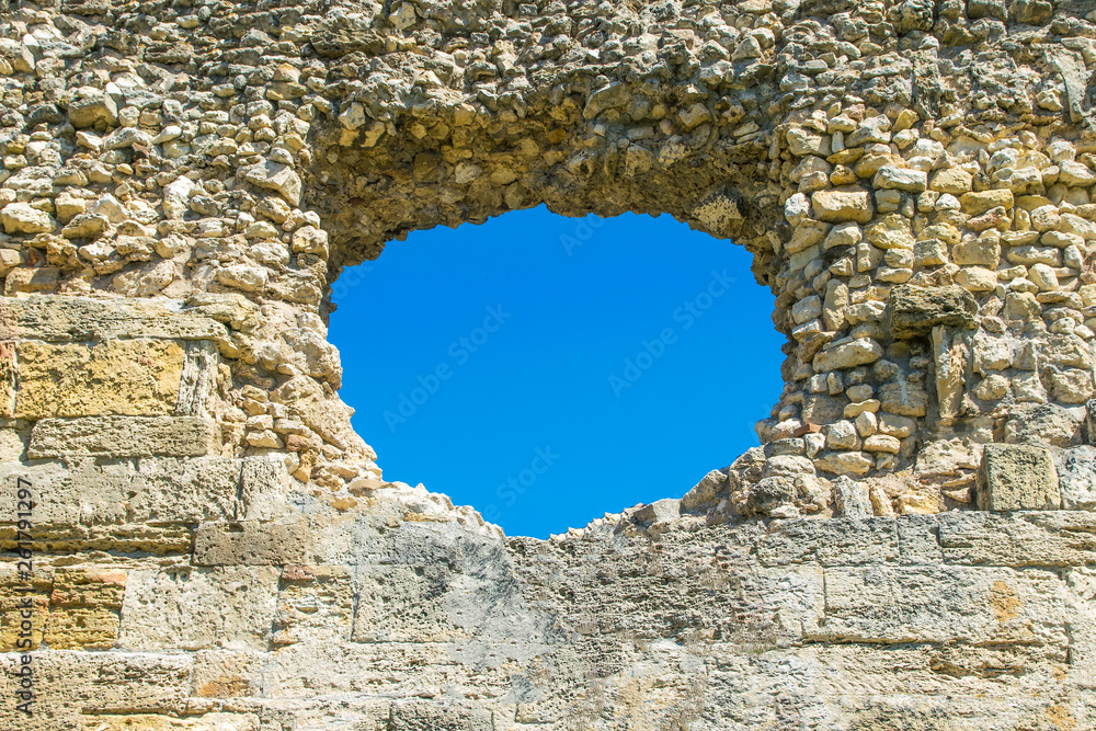 A hole in the stone wall and the blue sky in the background, a ruined wall with a hole. The image can be used as a background