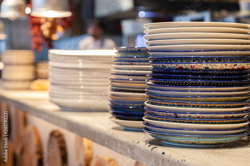 Closeup stack white and colored blue porcelain plates with oriental and ethnic ornament stands in open kitchen of trendy restaurant. Concept washing dishes, preparing for lunch, evening service